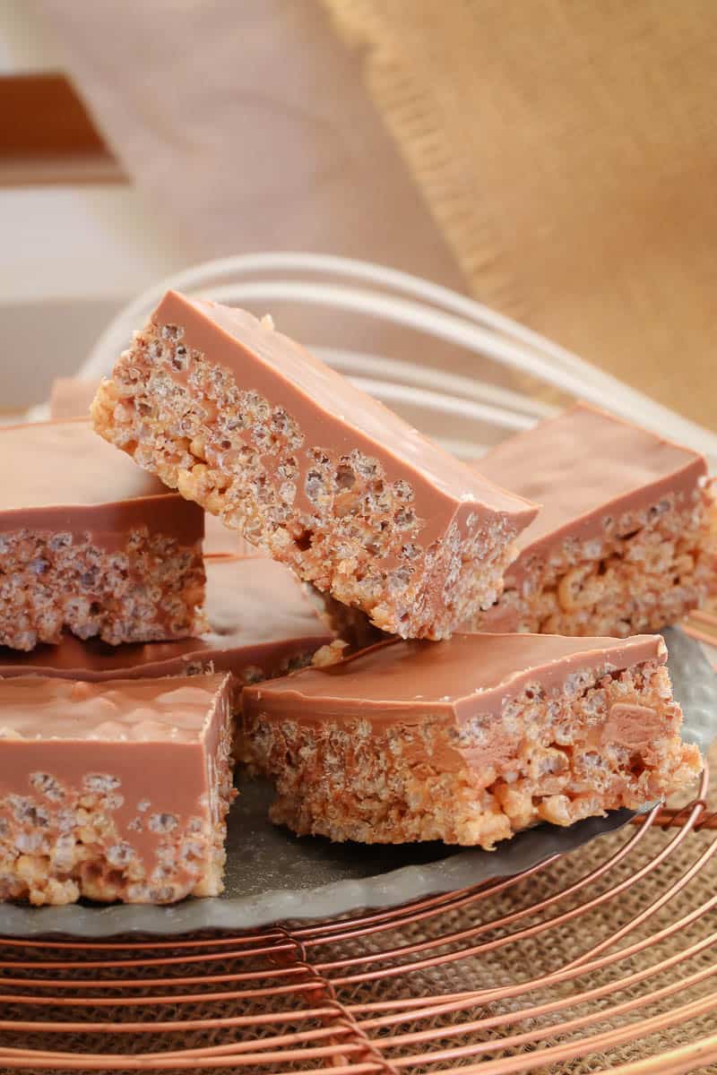 Pieces of chocolate slice made with Mars Bars and rice bubbles and topped with milk chocolate on a copper wire tray