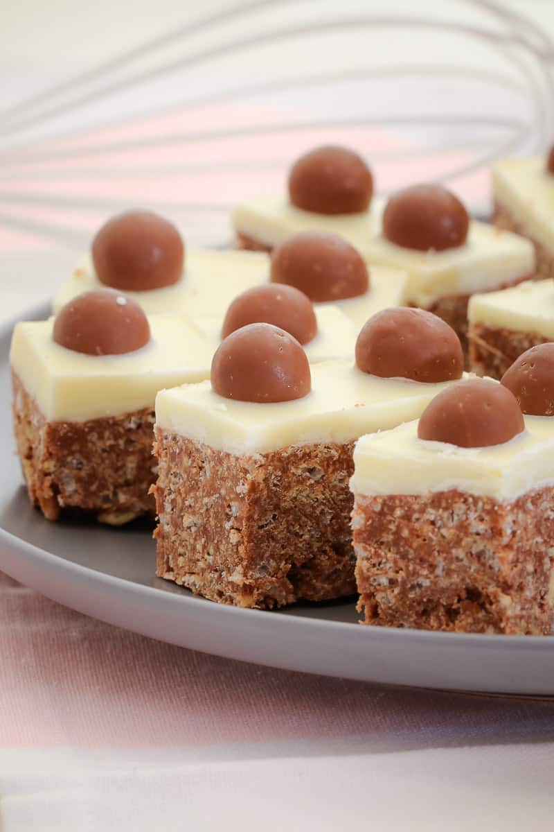 A plate of Malteser Slice with white icing and decorated with a Malteser on top of each slice.