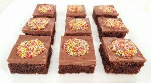 Squares of a chocolate slice lined up, with chocolate frosting and a Freckle on top of each piece