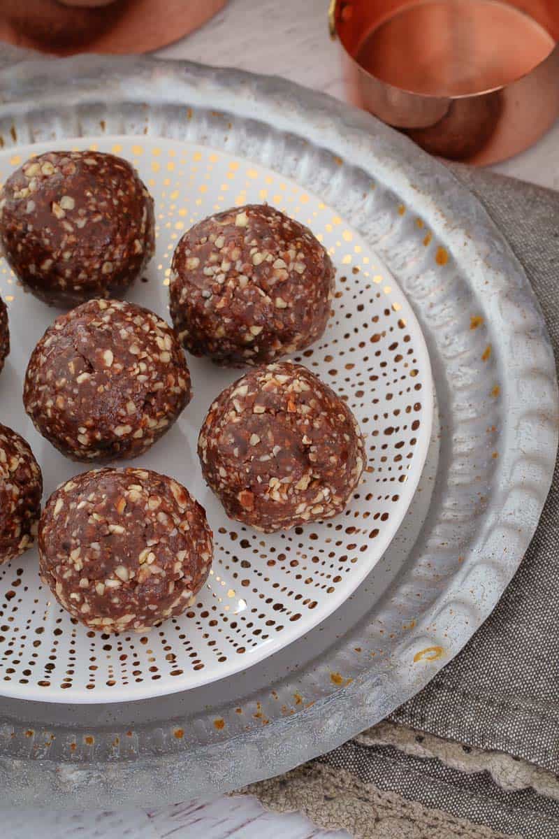 Almond, date, peanut butter and cacao protein balls on a plate next to a copper measuring cup