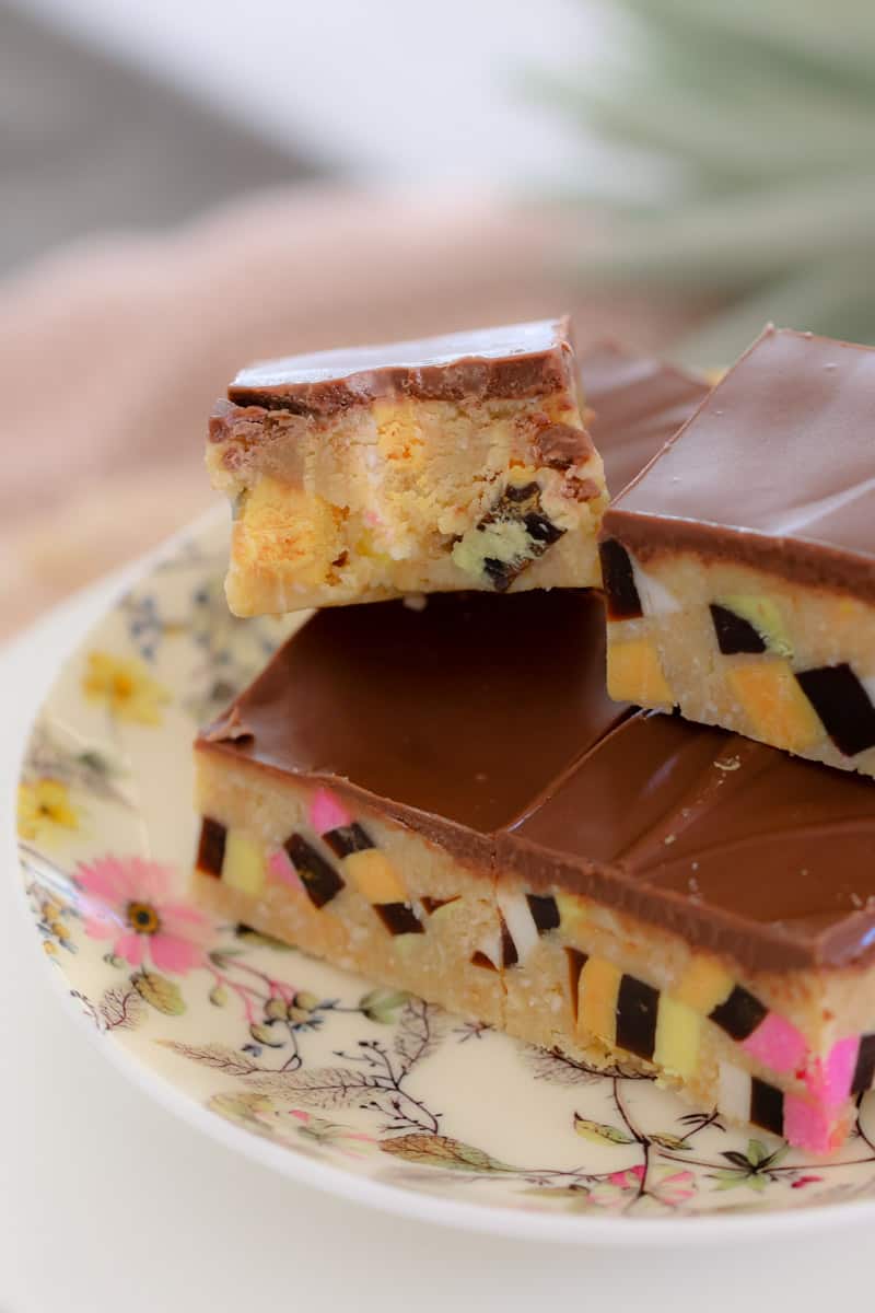 Pieces of a chocolate topped slice, served on a pretty floral plate, with a half eaten piece on top