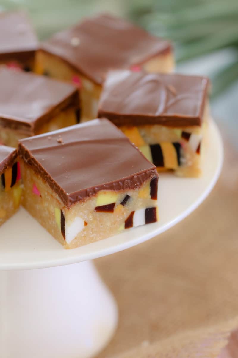 A close up of pieces of slice filled with chopped licorice allsorts and topped with chocolate on a white cake stand