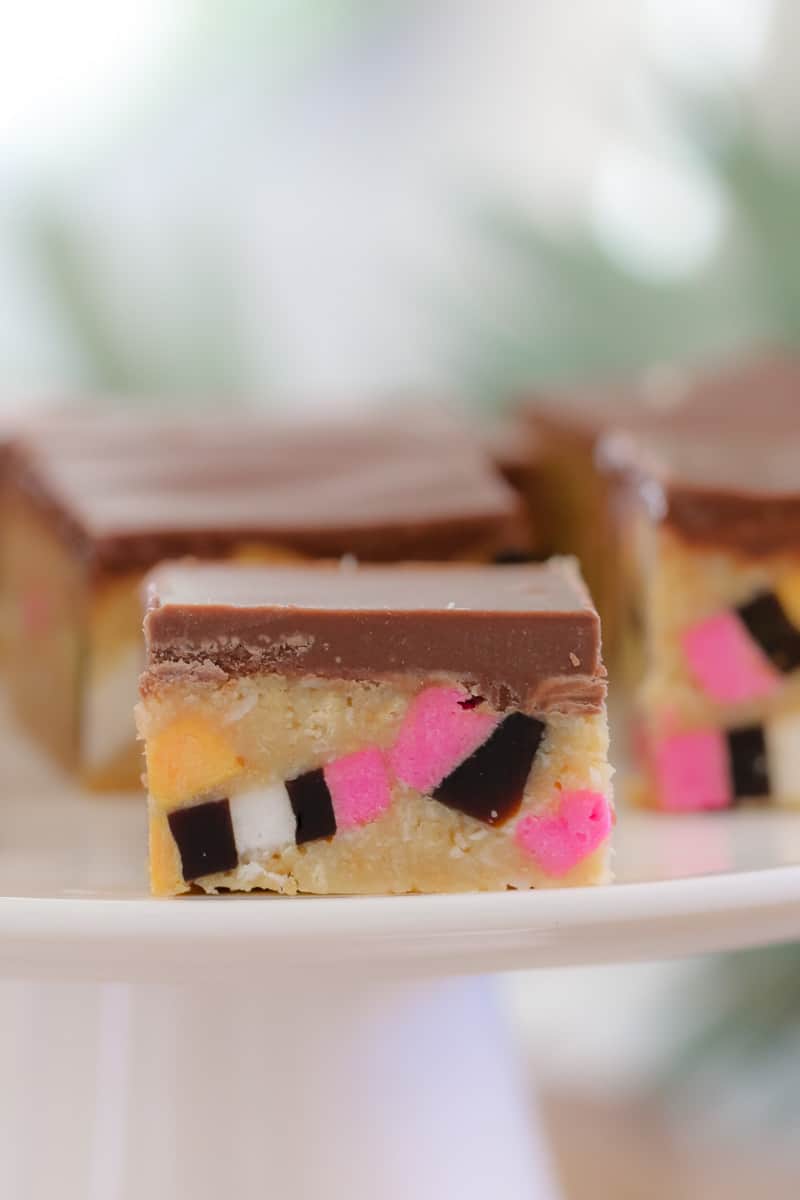 A side view of slice squares filled with colourful bits of licorice sweets and topped with chocolate