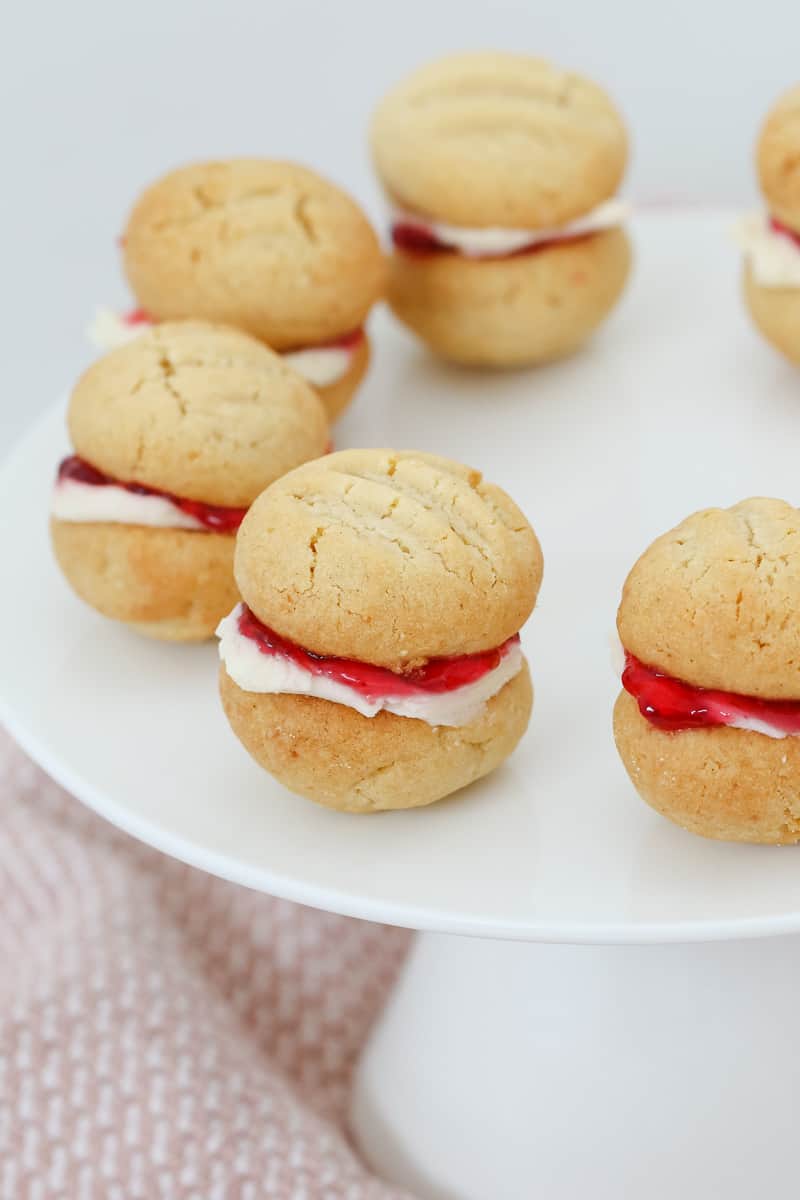 Coconut biscuits on a white plate sandwiched together with strawberry jam and white buttercream. 