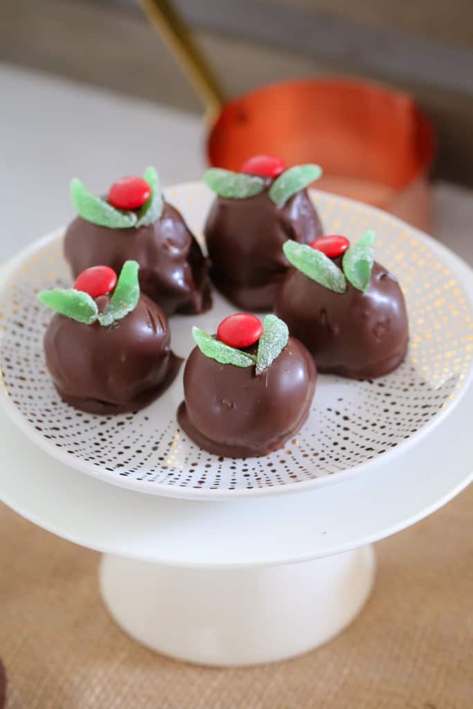 A plate of chocolate cheesecake balls decorated with slices of spearmint leaves and a red M&M to resemble mini Christmas Puddings