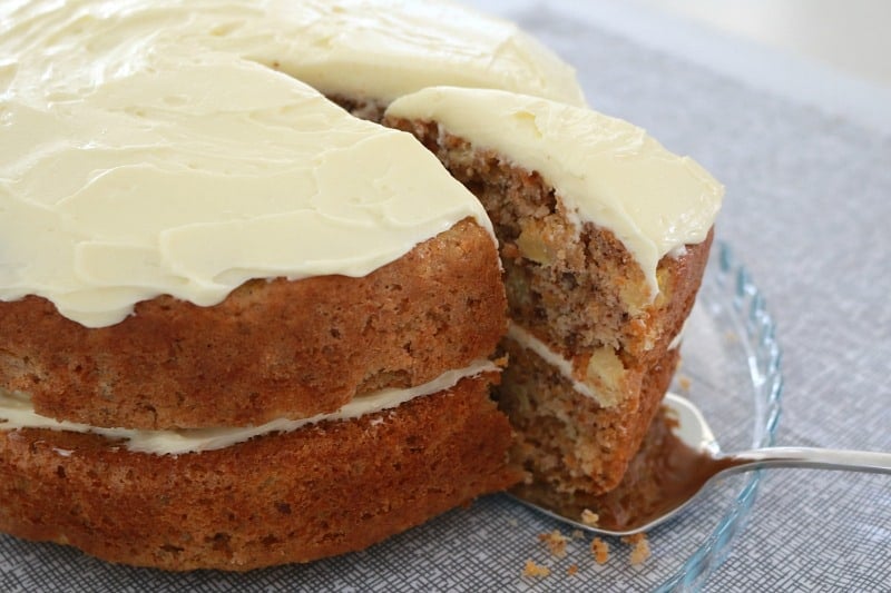 A slice of carrot cake with pecans being lifted from a cake