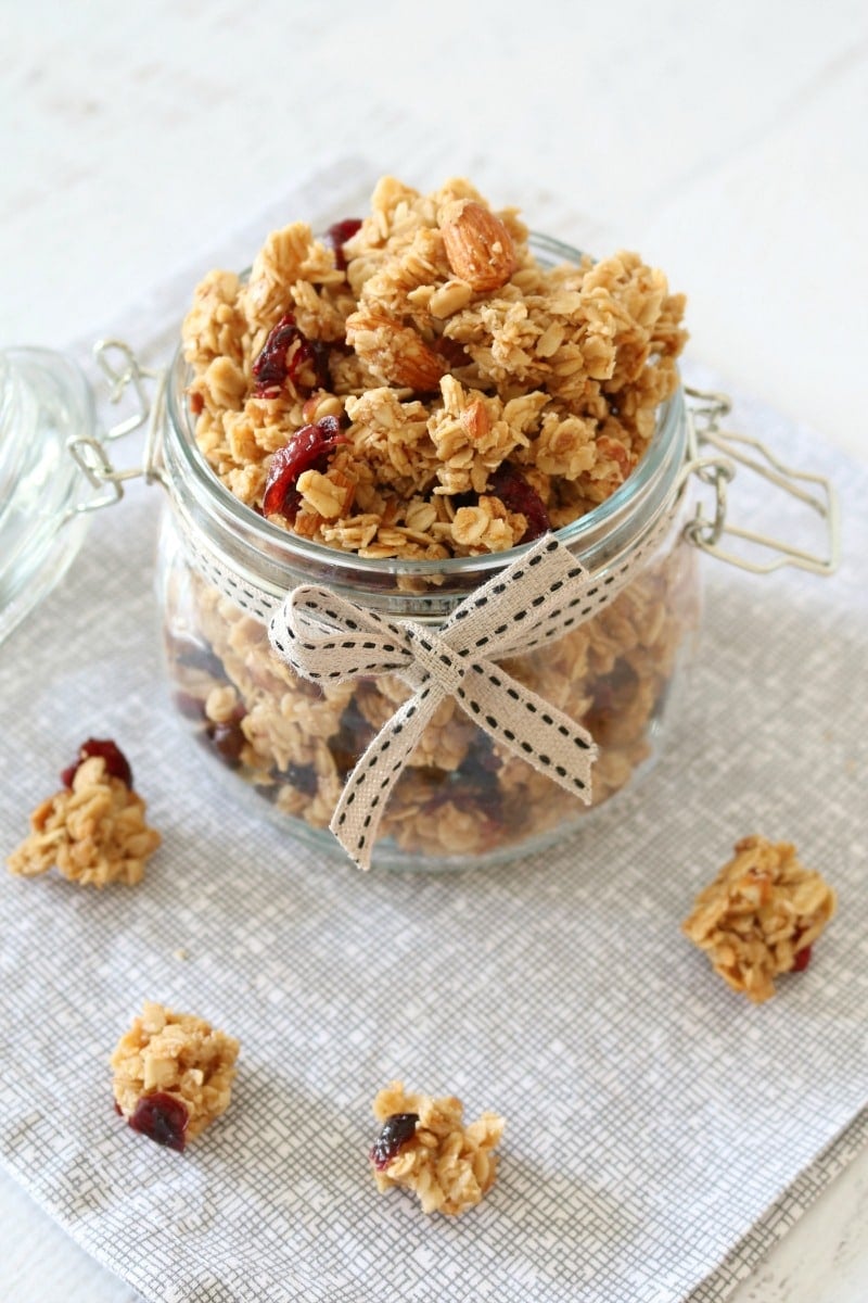A glass jar tied with a ribbon and filled with granola clusters with dried cranberries and almonds. 
