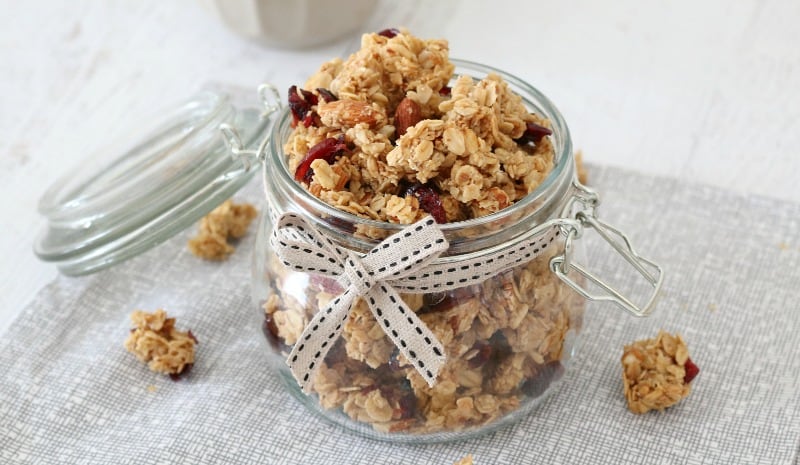A glass jar with a black and white ribbon tied around it, filled with clusters of homemade granola.