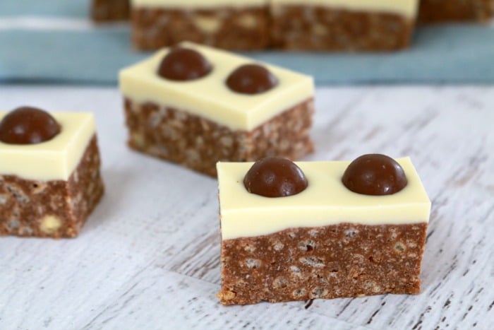 Pieces of a chocolate Malteser slice with a white chocolate topping and decorated with Maltesers on top