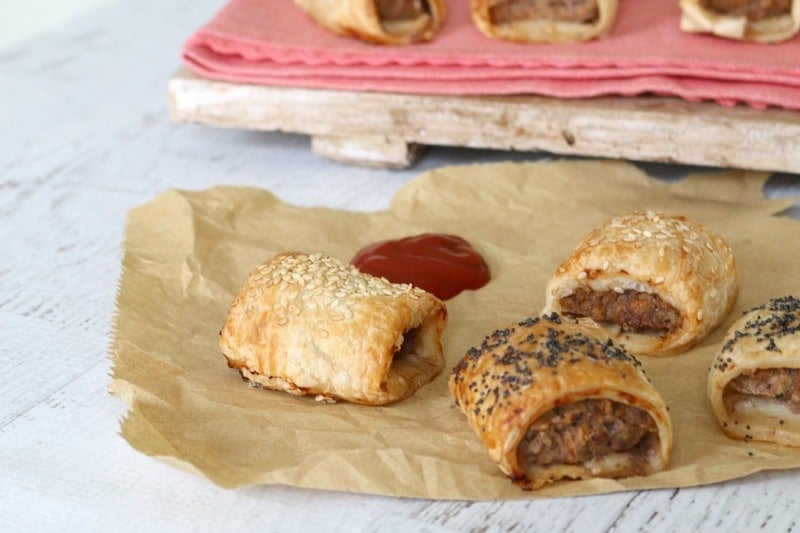 Three mini beef sausage rolls on brown paper served with a dollop of tomato sauce