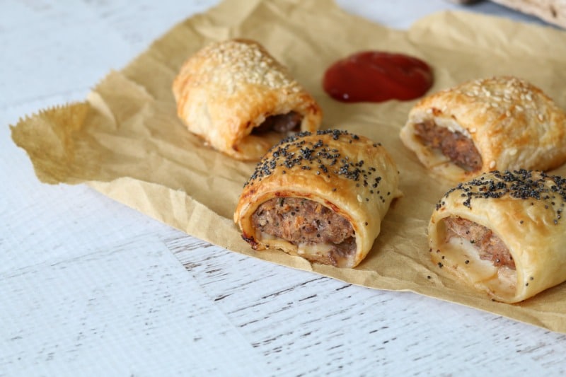 Mini sausage rolls sitting on brown paper with a dollop of tomato sauce beside