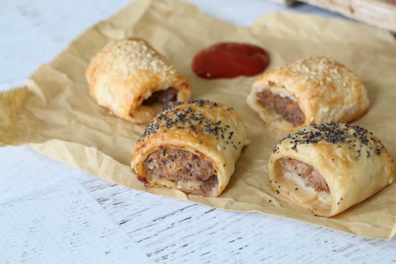 Sausage rolls on a sheet of brown paper, served with a splash of tomato sauce