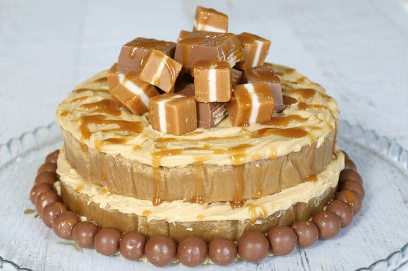 A round mud cake drizzled with caramel sauce and decorated with a pile of Jersey Caramels on top, and Maltesers around the base