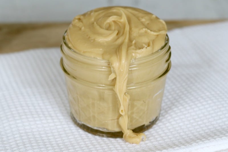A glass jar filled with a pale salted caramel frosting, with some frosting split down the front of the jar