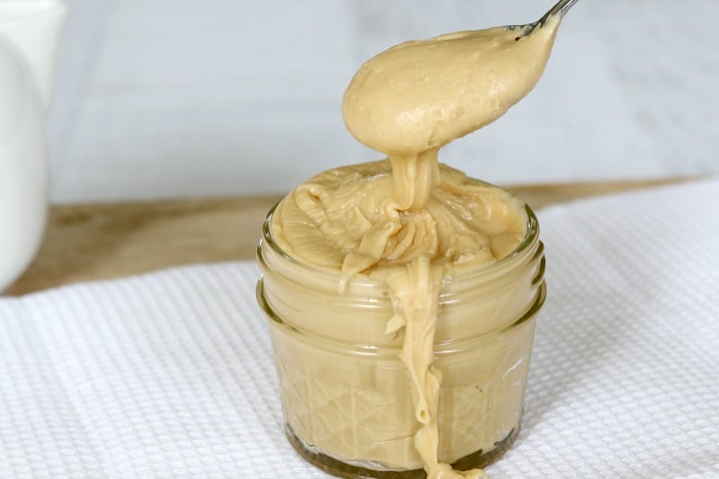 A spoonful of salted caramel frosting held above a small glass jar filled with frosting