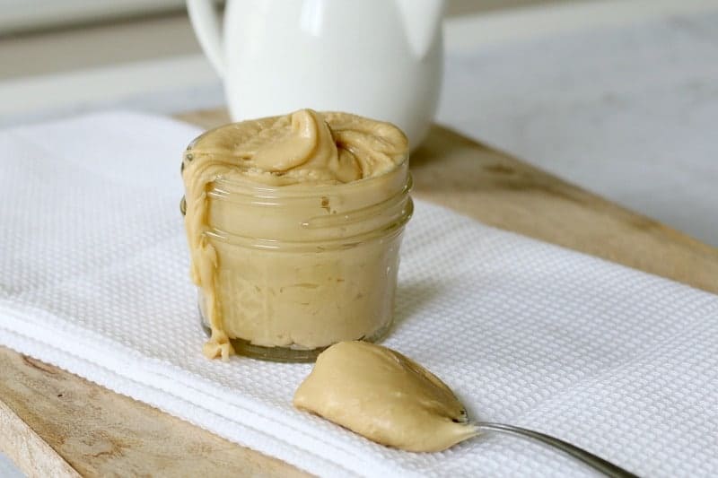 A small glass jar filled with thick salted caramel frosting, with a spoonful of frosting resting beside