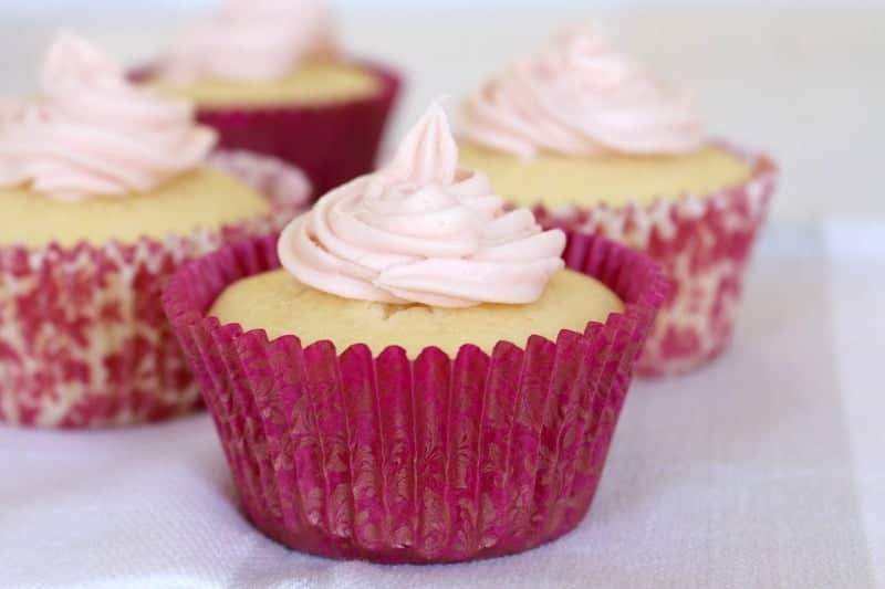 A close up of cupcakes in pink cases with swirls of white frosting on top