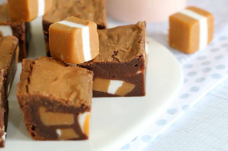 Pieces of a chocolate brownie showing chunks of Jersey Caramel inside, and some Jersey Caramel sweets sitting on top.
