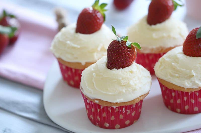 Fresh strawberries on top of white frosting on vanilla cupcakes in pink cases