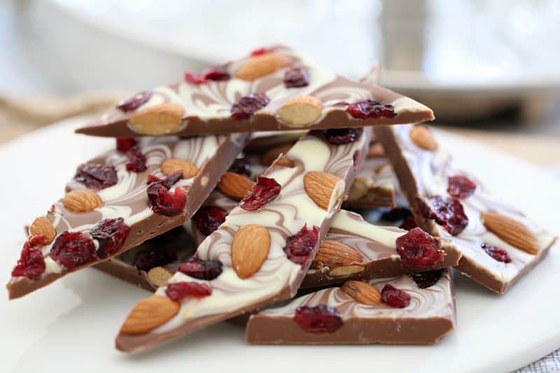 Roasted almond and cranberry chocolate bark shard on a white plate.