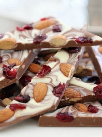 A stack of chocolate bark topped with white chocolate and decorated with roasted almonds and cranberries.