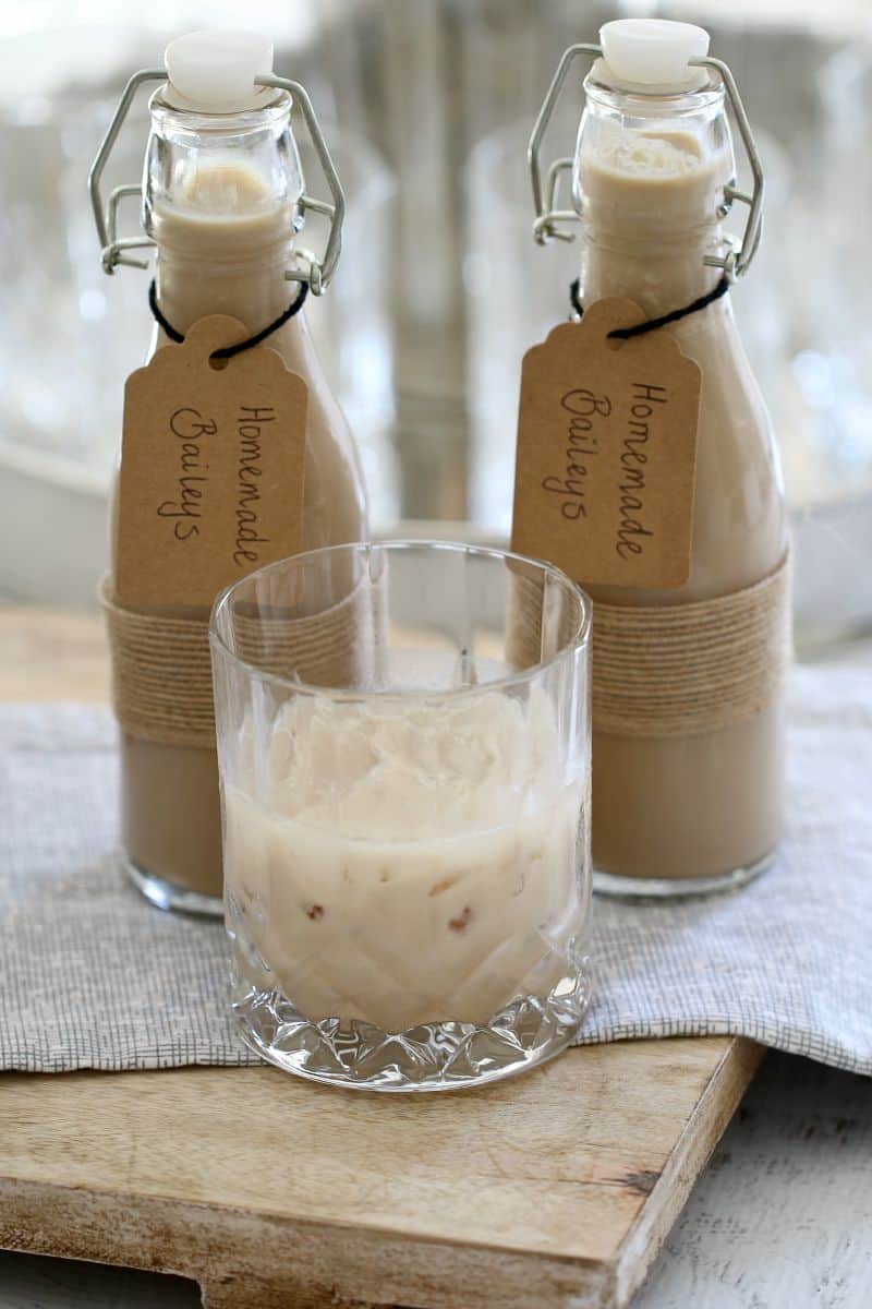 Homemade Baileys Irish Cream in small labelled bottles next to a glass of Baileys over ice