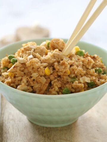 A pale blue bowl filled with fried rice, and a set of chopsticks placed in it