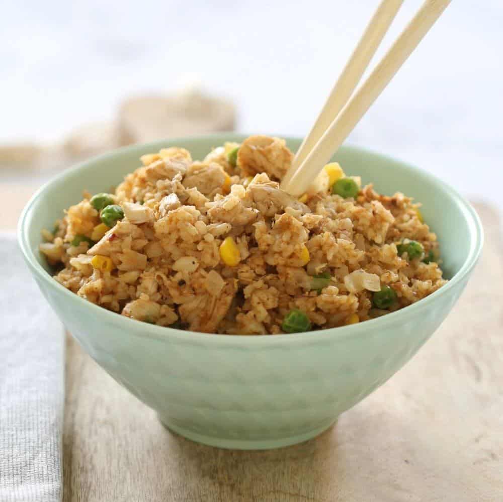 A pale blue bowl filled with fried rice, and a set of chopsticks placed in it