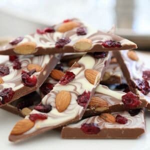A stack of chocolate bark topped with white chocolate and decorated with roasted almonds and cranberries