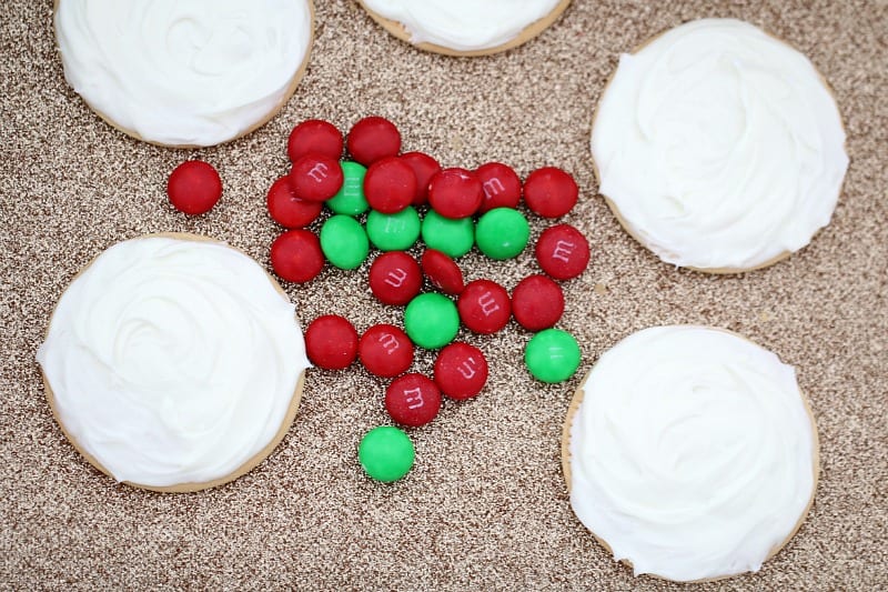 Biscuits iced with white frosting and red and green M&M\'s on a bench