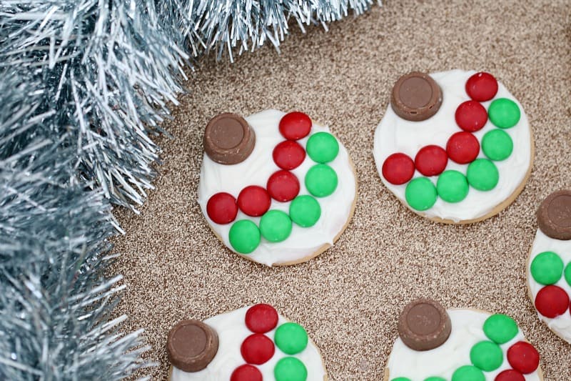Christmas bauble biscuits with white frosting, a chocolate and red and green M&M\'s, on a bench