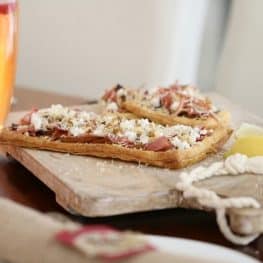 Flat oblong pastry tarts topped with pear, prosciutto and goats cheese and served on a wooden board