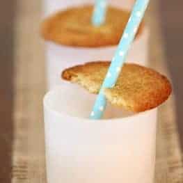 A close up of a half eaten Snickerdoodle cookie on the top of a white glass with a drinking straw