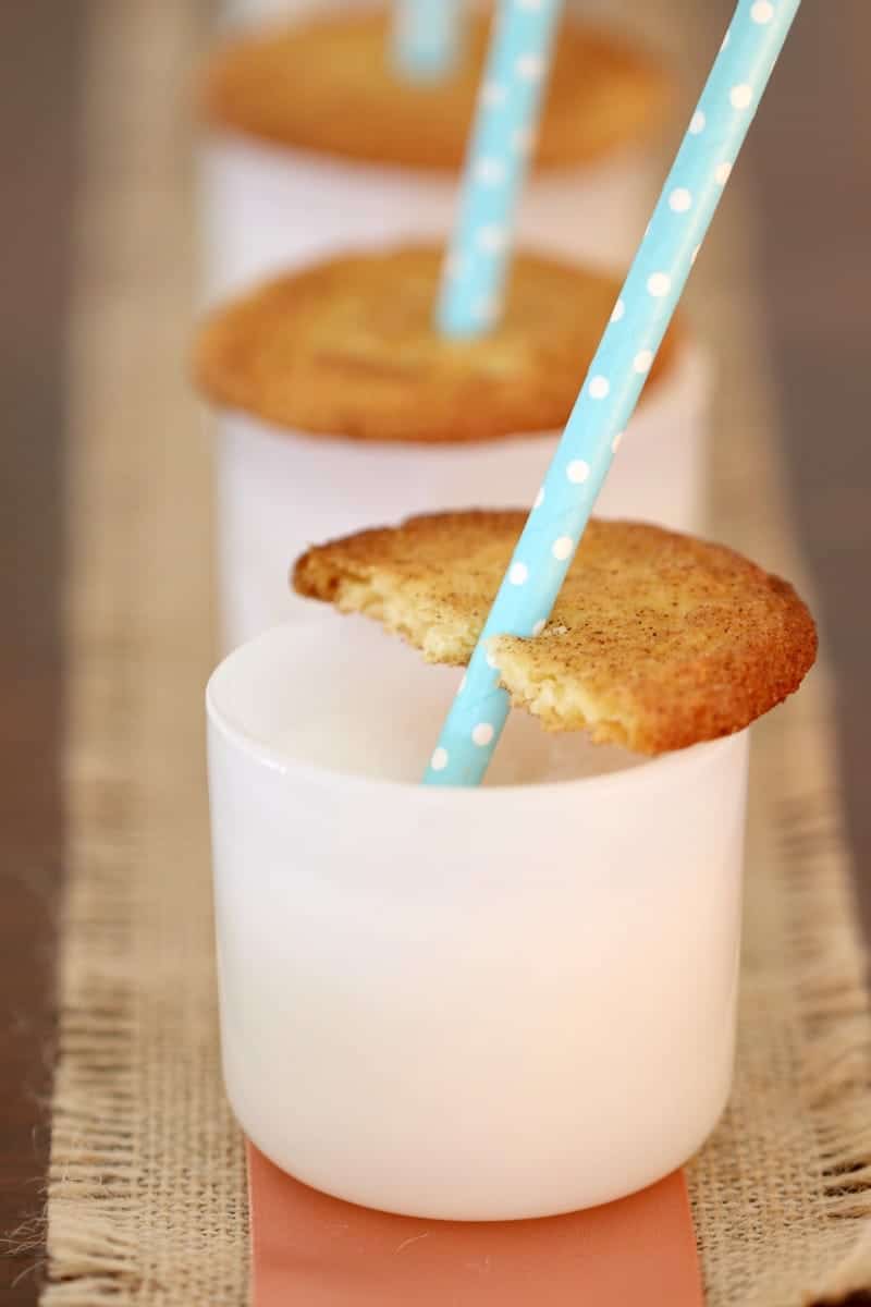 A close up of a half eaten Snickerdoodle cookie on the top of a white glass with a drinking straw