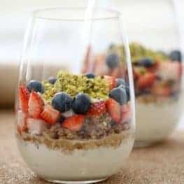 A stemless wine glass filled with layers of yoghurt, oats, berries, nuts and spices