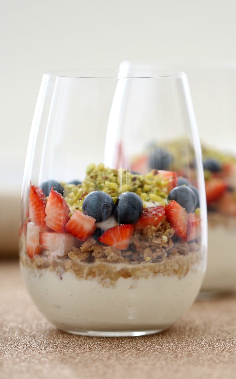 A stemless wine glass with a bottom layer of yoghurt, then chopped strawberries and blueberries and an oat granola