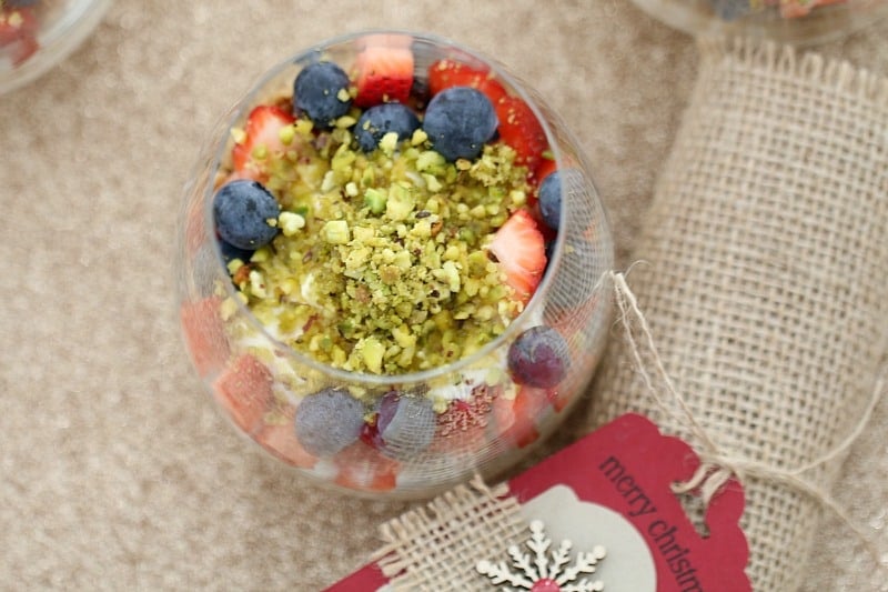 An overhead shot of a glass filled with yoghurt, granola, mixed berries and crushed pistachios