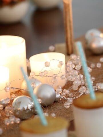 Christmas decorations, candles, and cookies with a straw through them on top of white glass jars