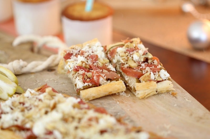 Cut pieces of a pastry tart baked with goats cheese, prosciutto and slices of pear, on a wooden board