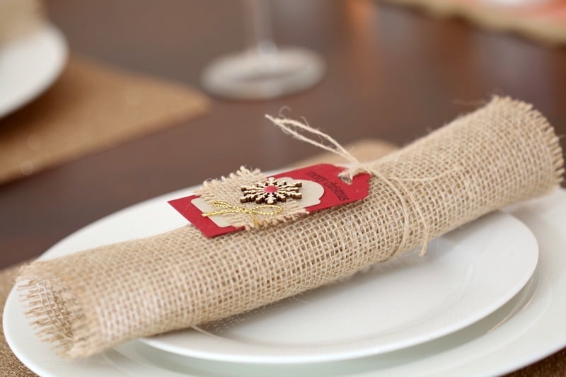 A hessian napkin rolled up and tied with a Christmas label, placed on a white plate