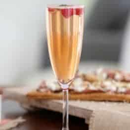 A long stemmed champagne glass filled with sparkling wine, liqueur, raspberries and mint leaves