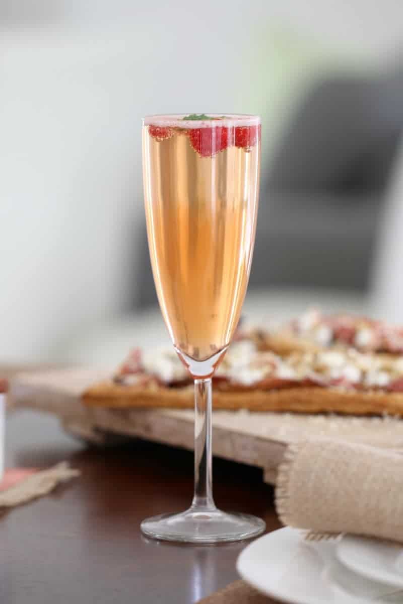 A long stemmed champagne glass filled with sparkling wine, liqueur, raspberries and mint leaves