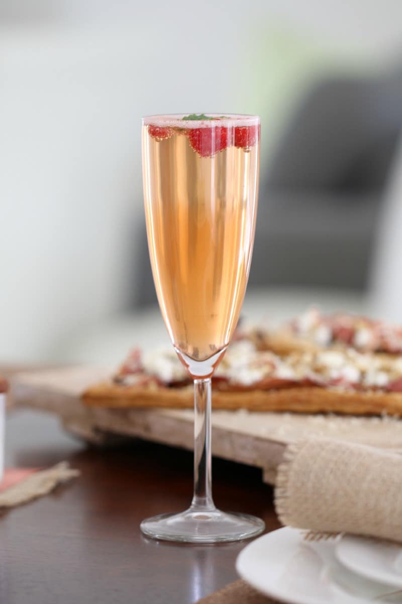 A long stemmed champagne glass filled with sparkling wine and liqueur, and topped with strawberries and mint