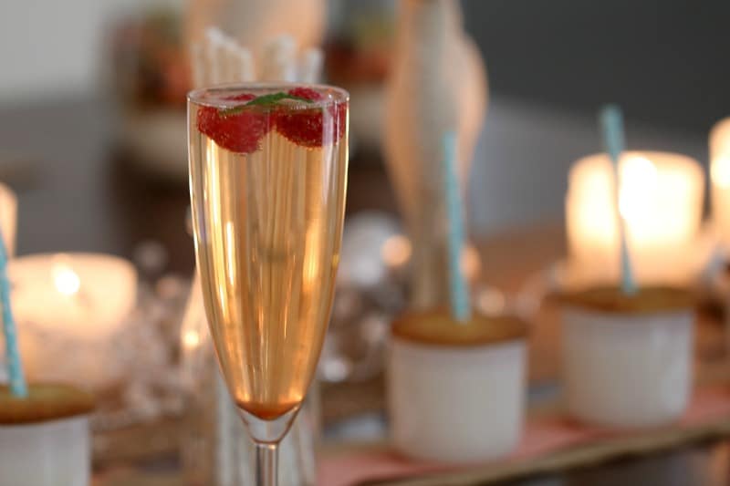 A close up of a champagne glass filled with sparkling wine, with chopped strawberries and mint on top