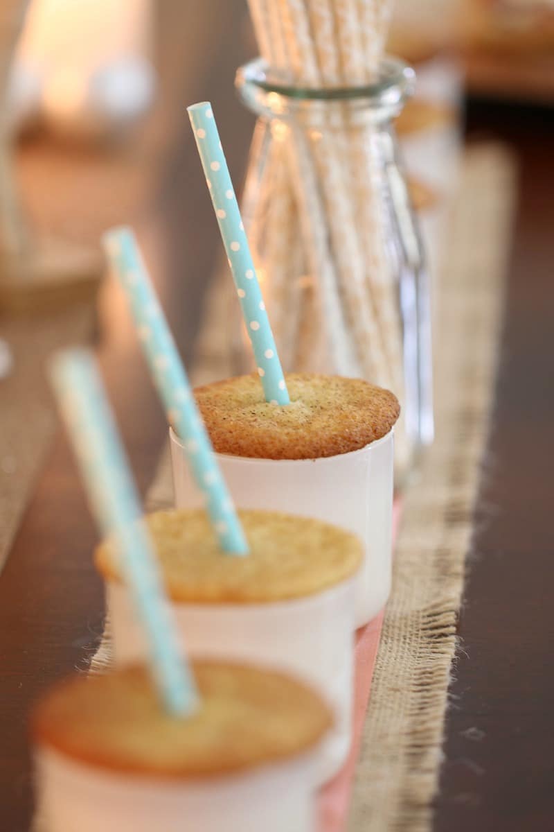 A close up of spiced cookies placed on the top of white glass jars and a straw through the middle of them
