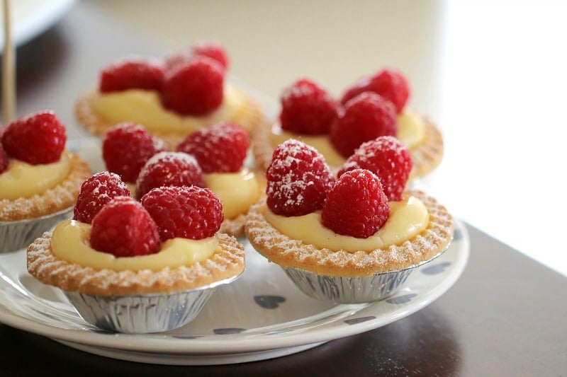 Mini vanilla custard tarts topped with raspberries, in silver foil cases