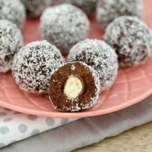 Malteser balls covered in coconut on a pink plate, with one bitten in half to show texture inside