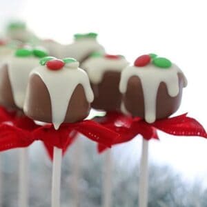 Sticks of chocolate coated truffles tied with a red ribbon and decorated with white chocolate and green and red sweets.