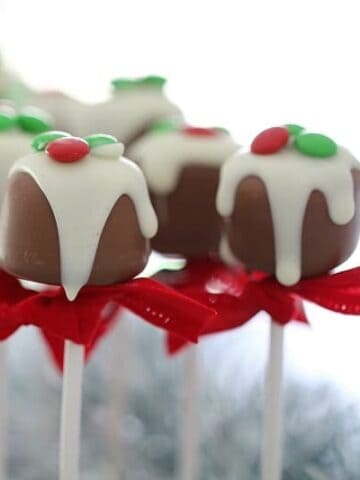 Sticks of chocolate coated truffles tied with a red ribbon and decorated with white chocolate and green and red sweets.