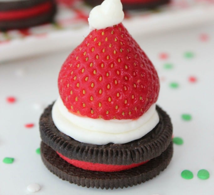 An Oreo biscuit with icing and a fresh strawberry on top to resemble a red Santa hat
